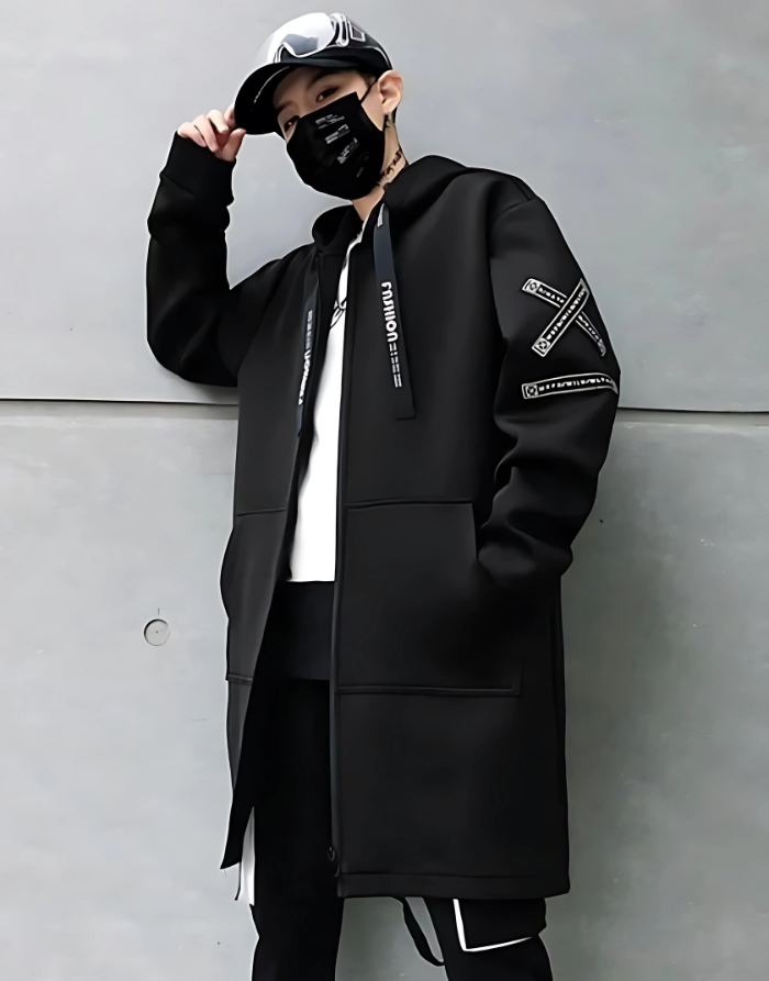 Person wearing a black coat with brand logos against a gray wall