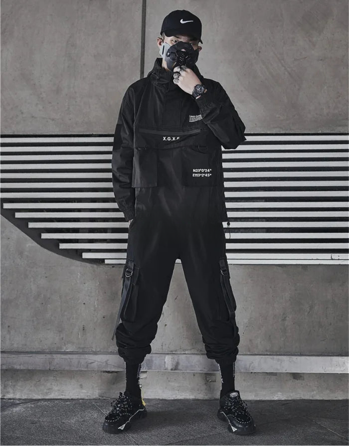 Person wearing a black outfit with text, standing against a concrete wall with horizontal lines.