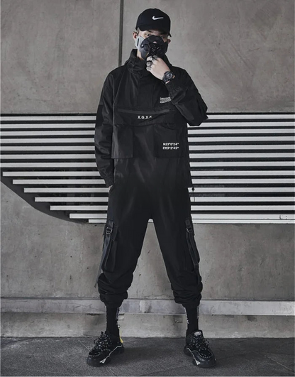 Person wearing a black outfit with text, standing against a concrete wall with horizontal lines.