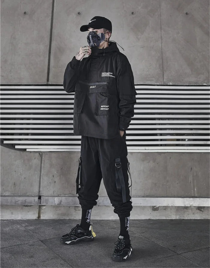 Person wearing a black outfit with tactical pants and a cap, standing against a concrete wall with horizontal stripes.