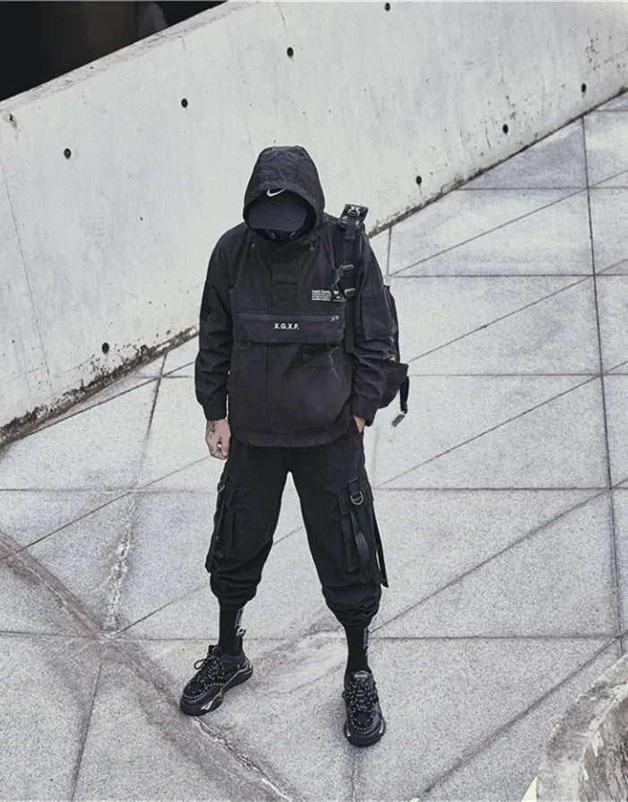 Person wearing a black outfit with a backpack against a concrete wall.