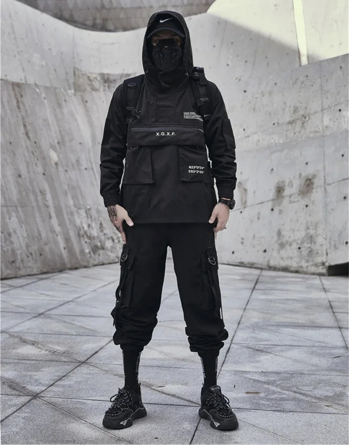 Person wearing a black tactical outfit with a hood in an urban setting.